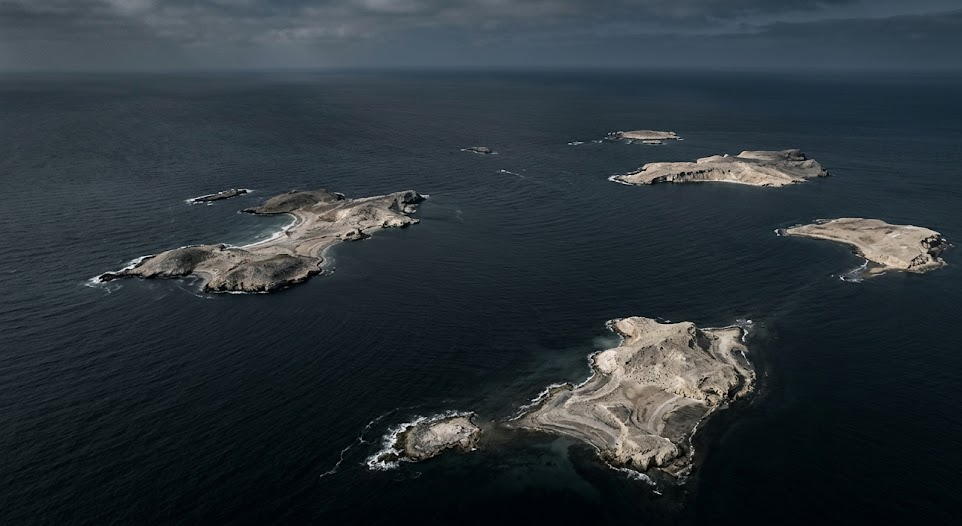 Aerial view of sparse pale islands in a dark ocean